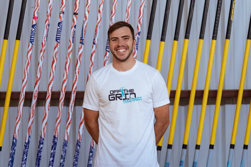 Off The Grid Pole Vault head coach in front of the pole rack